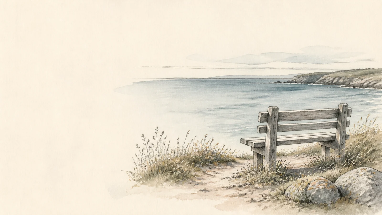 An empty wooden bench overlooking a quiet Cornish sea.
