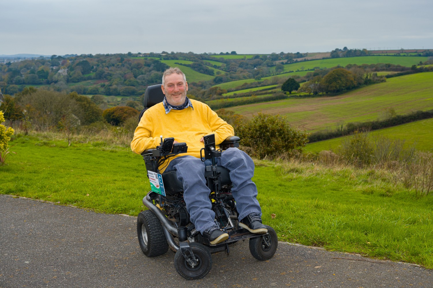 Steven Webb in his electric wheelchair, with green fields behind him